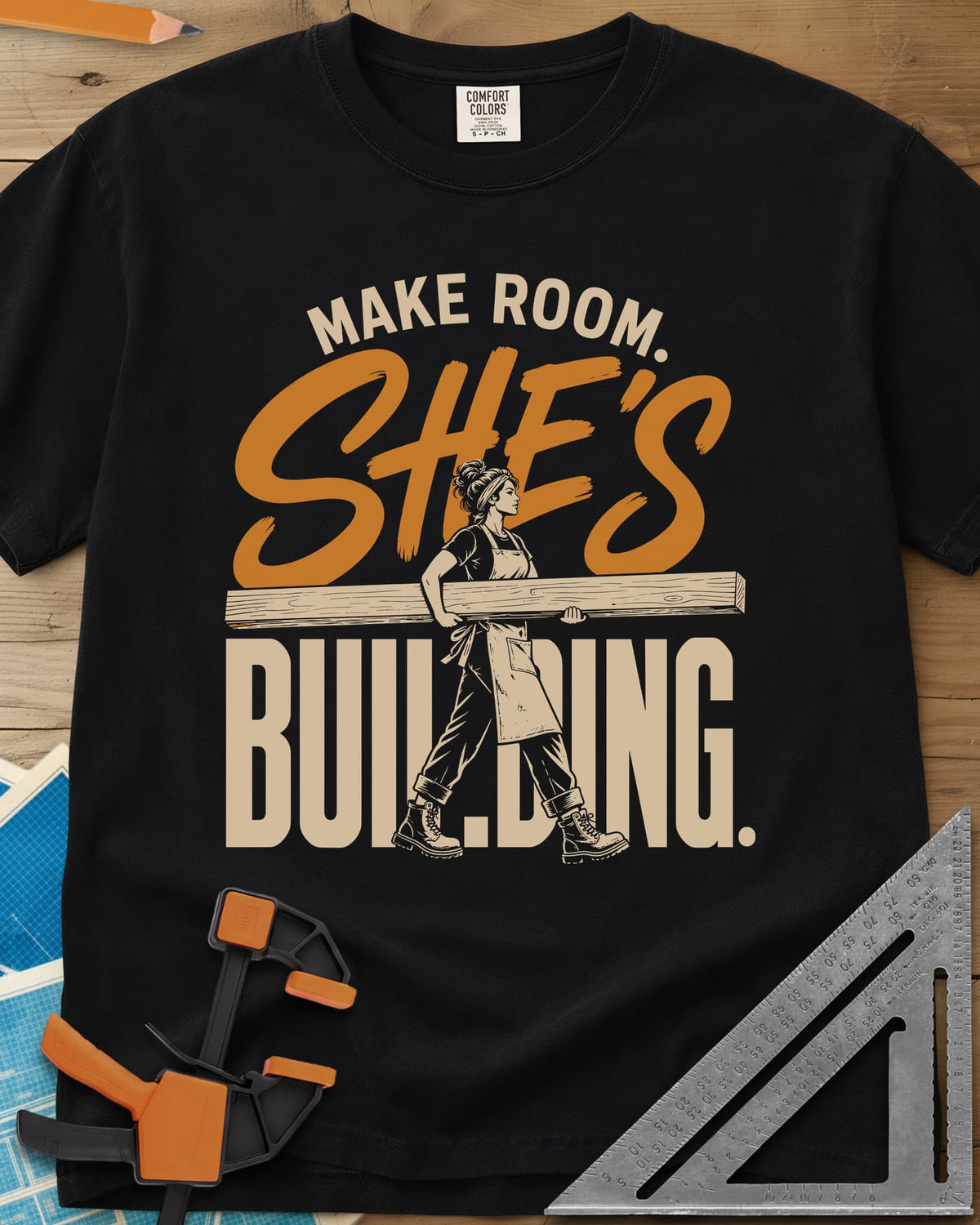 She'S Building heavyweight tee in Black, a woman in boots carrying a long beam through the lettering