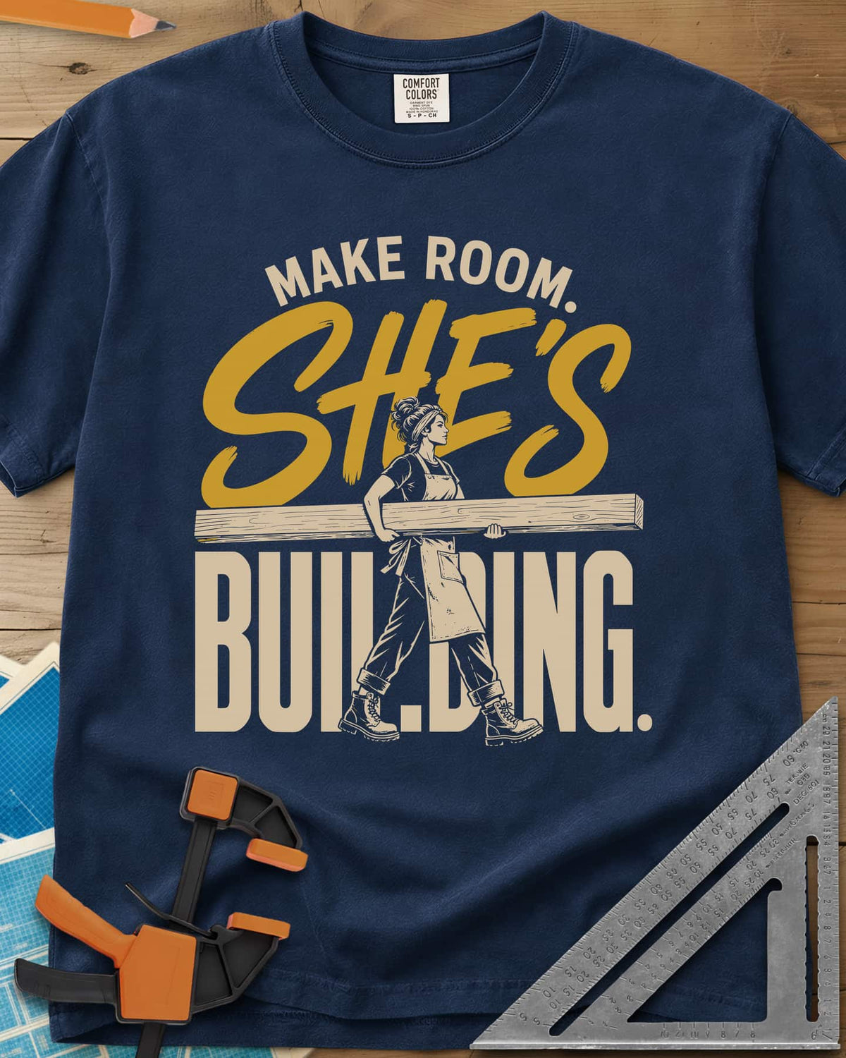She'S Building heavyweight tee in Navy, a woman in boots carrying a long beam through the lettering