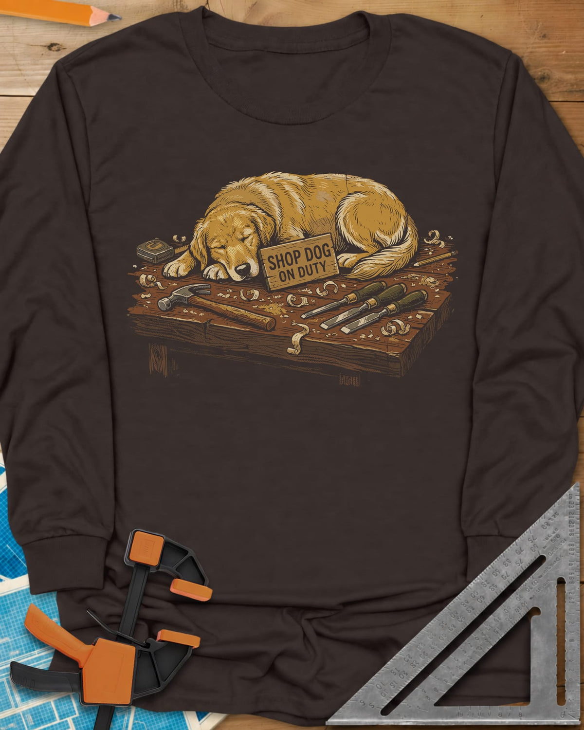 Shop Dog On Duty long sleeve shirt in Dark Chocolate, a golden retriever asleep on a workbench beside tools and shavings