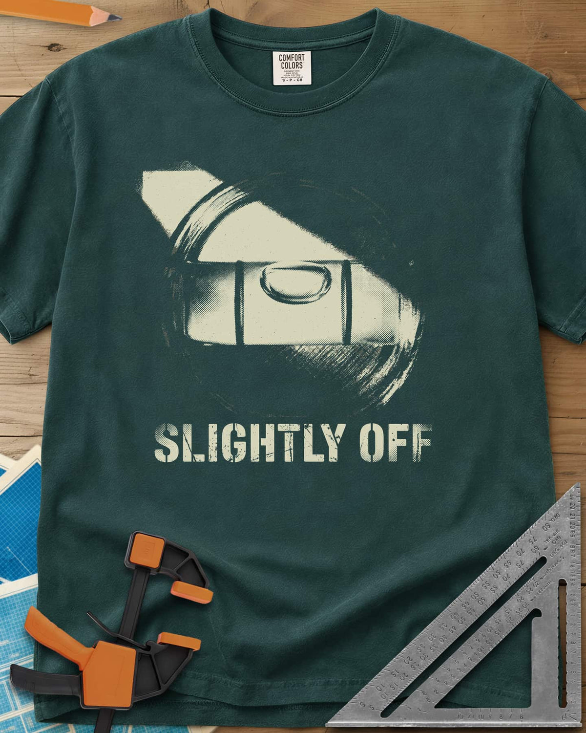 Slightly Off Level heavyweight tee in Blue Spruce, a tilted spirit level and its bubble vial in grainy halftone