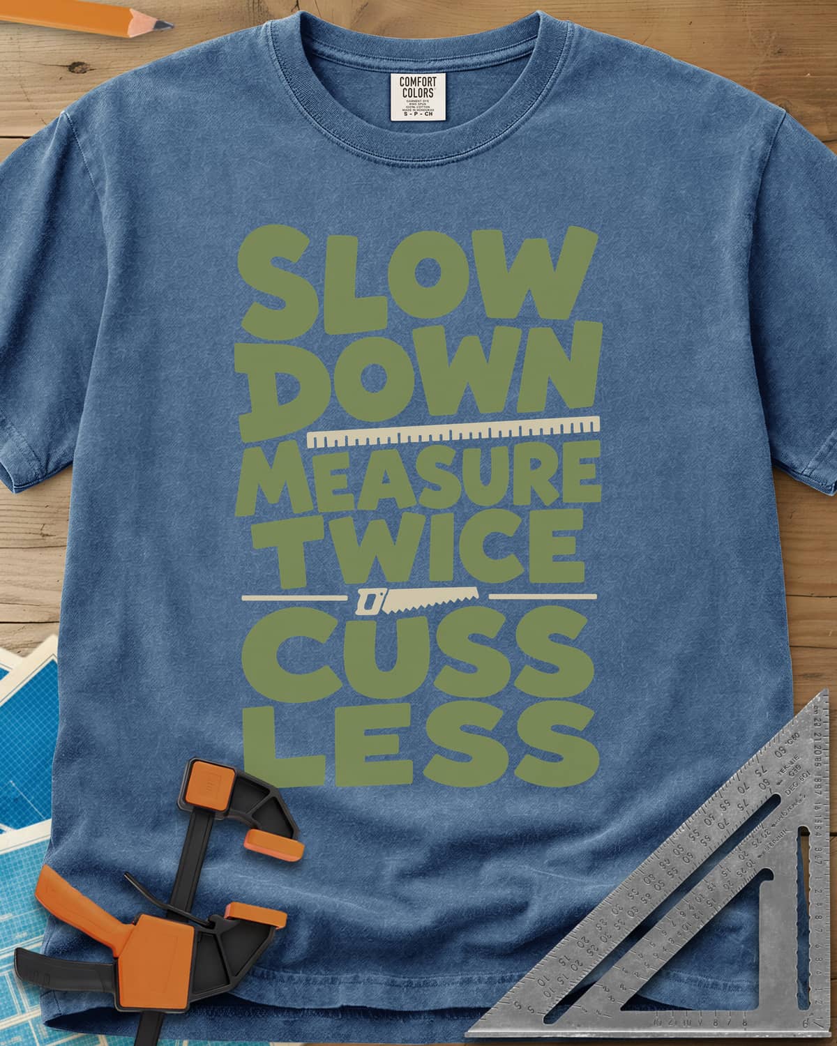 Slow Down Measure Twice heavyweight tee in Blue Jean, stacked green letters with a ruler and a small handsaw between lines