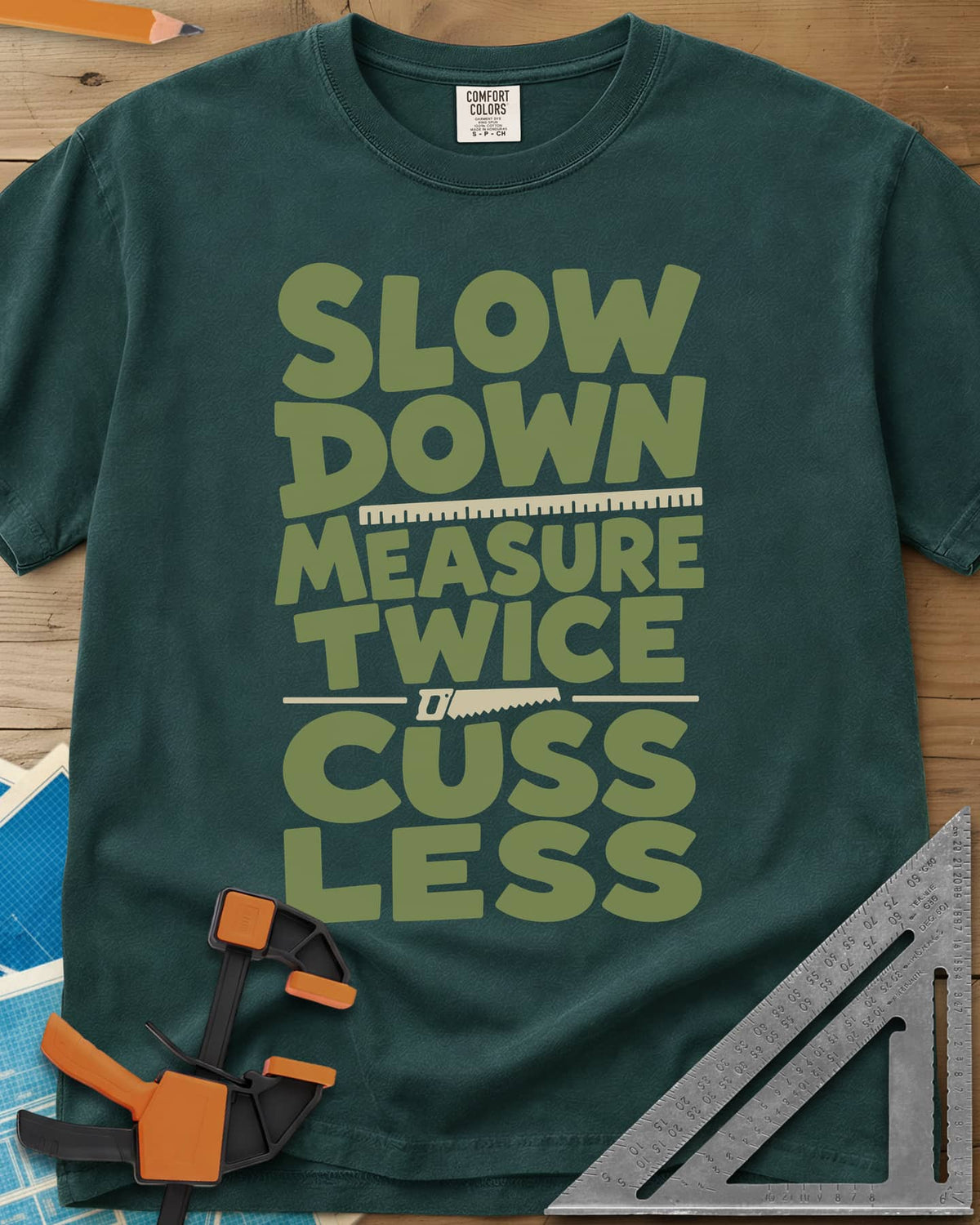 Slow Down Measure Twice heavyweight tee in Blue Spruce, stacked green letters with a ruler and a small handsaw between lines