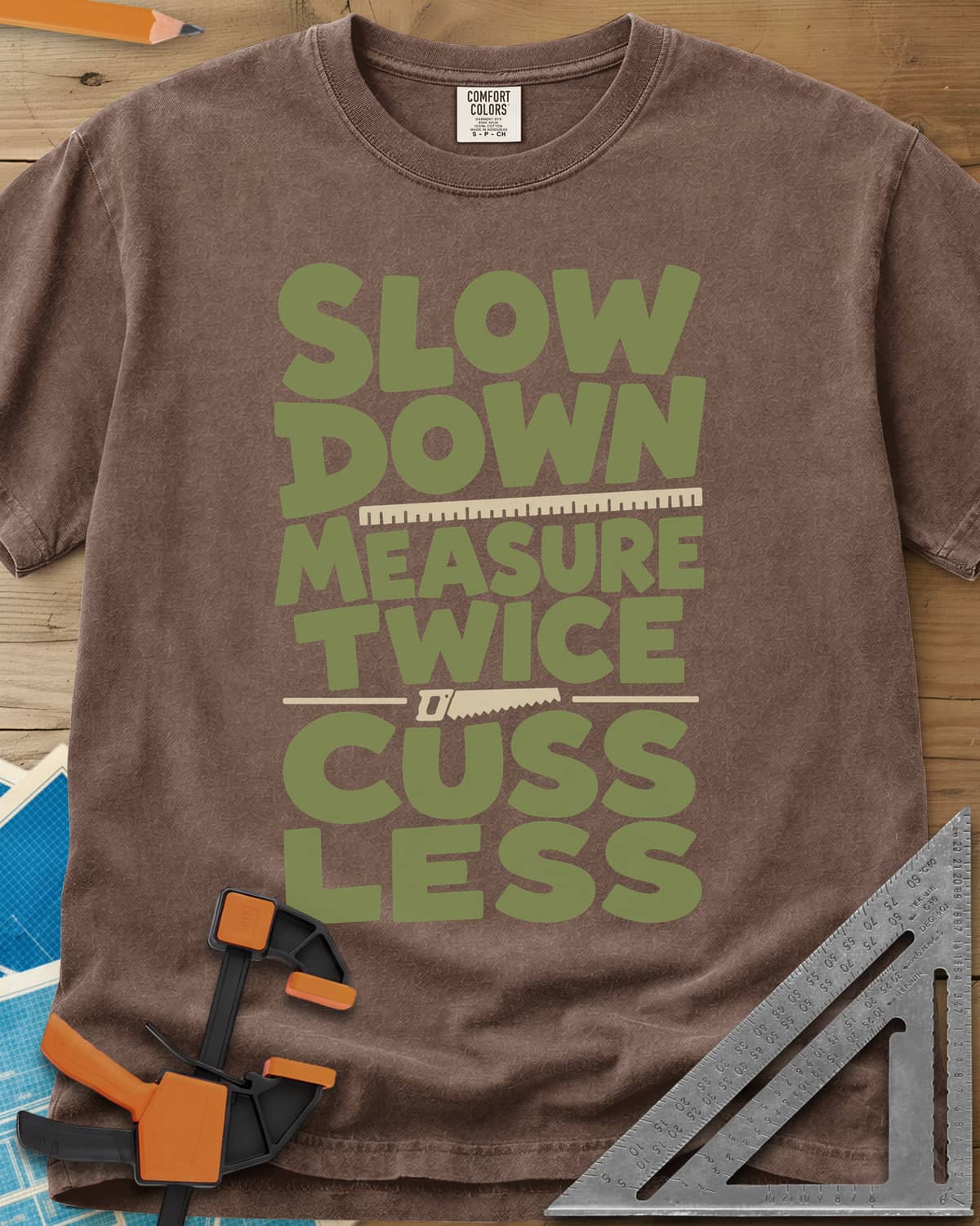 Slow Down Measure Twice heavyweight tee in Espresso, stacked green letters with a ruler and a small handsaw between lines