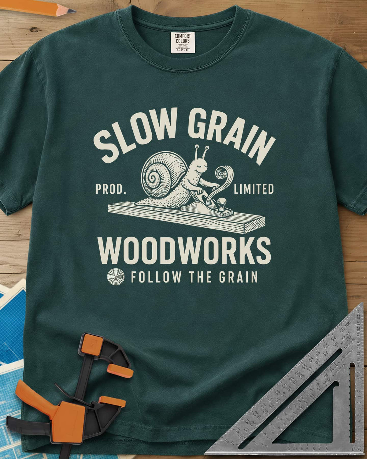 Slow Grain heavyweight tee in Blue Spruce, a smiling snail planing a plank, one curl of shaving rising