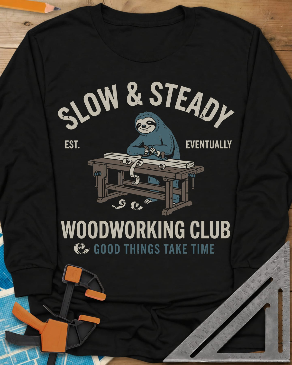 Slow Steady long sleeve shirt in Black, a blue sloth planing a board at a workbench, shavings falling