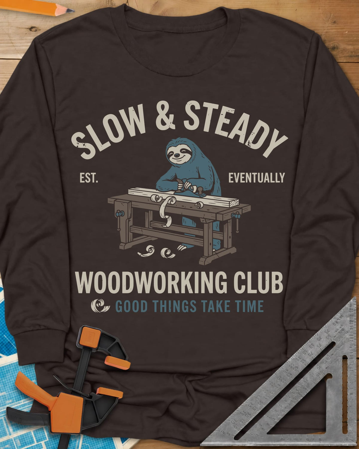 Slow Steady long sleeve shirt in Dark Chocolate, a blue sloth planing a board at a workbench, shavings falling