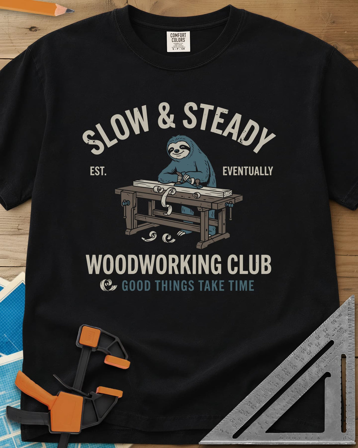 Slow Steady heavyweight tee in Black, a blue sloth planing a board at a workbench, shavings falling