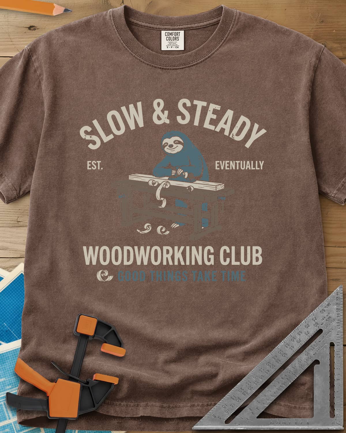 Slow Steady heavyweight tee in Espresso, a blue sloth planing a board at a workbench, shavings falling