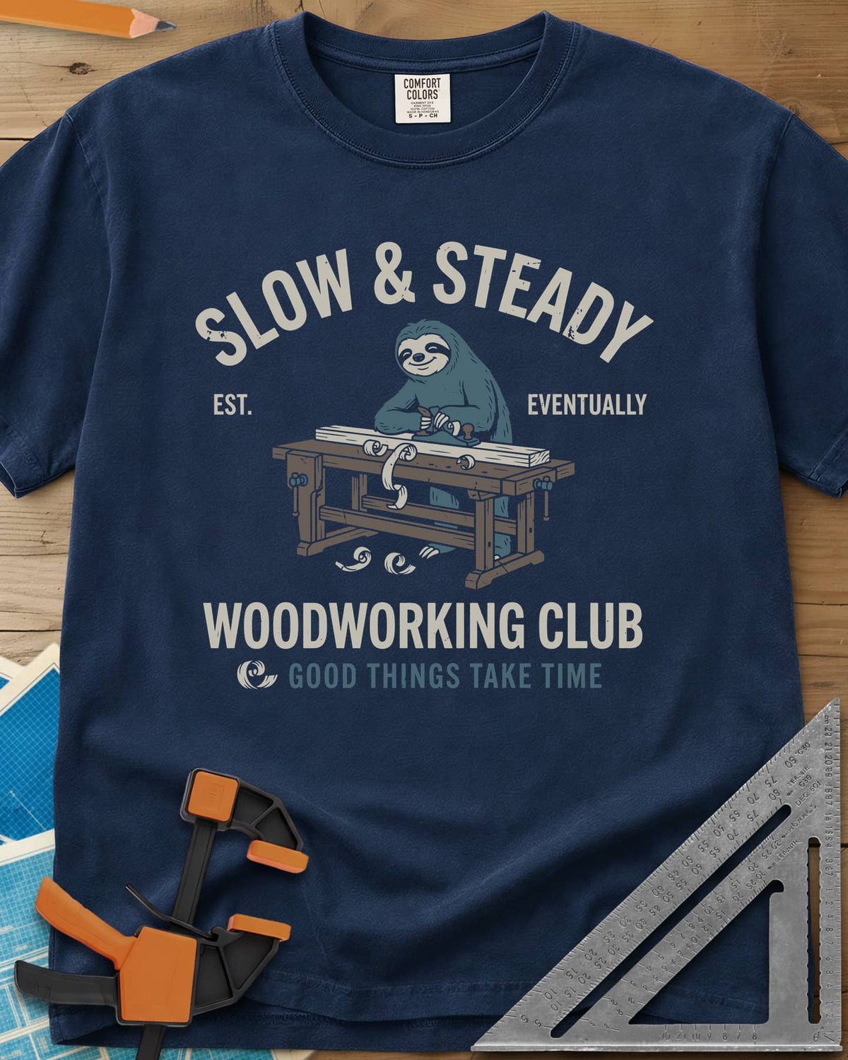 Slow Steady heavyweight tee in Navy, a blue sloth planing a board at a workbench, shavings falling