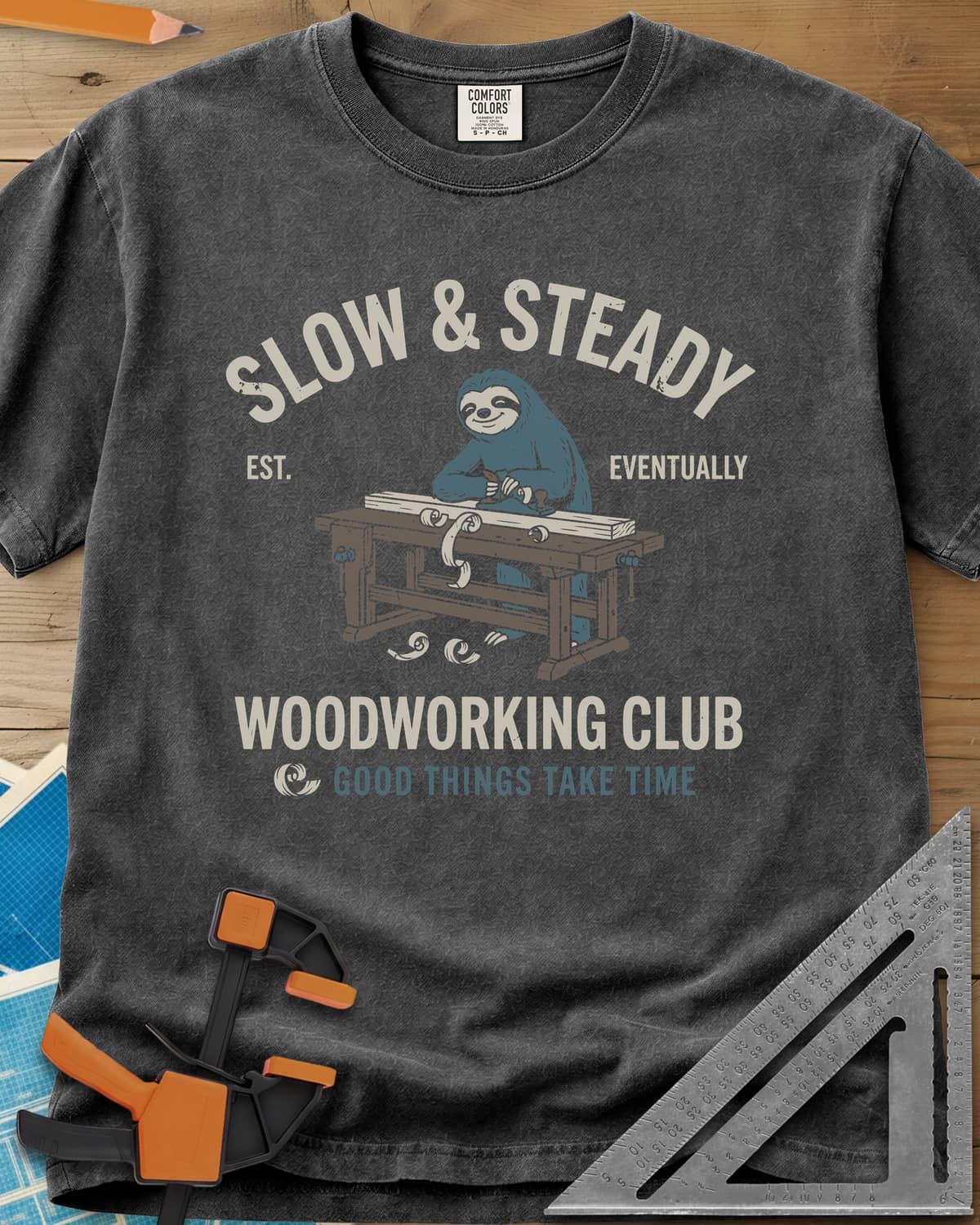 Slow Steady heavyweight tee in Pepper, a blue sloth planing a board at a workbench, shavings falling