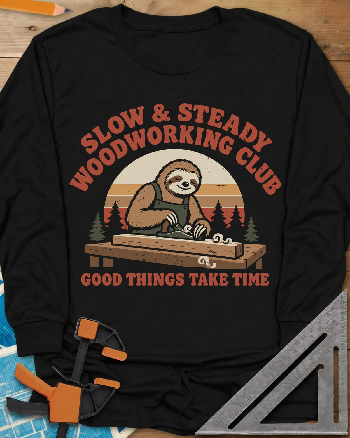 Slow Woodwork long sleeve shirt in Black, a sloth in overalls planing a board, retro sunset and pines