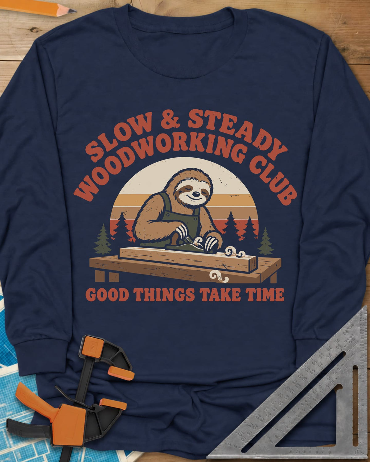 Slow Woodwork long sleeve shirt in Navy, a sloth in overalls planing a board, retro sunset and pines