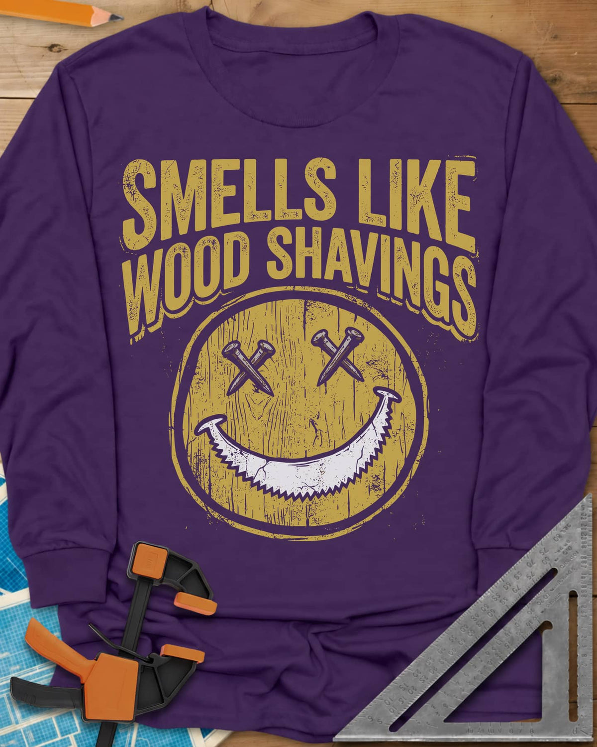 Smells Like Wood Shavings long sleeve shirt in Purple, a worn yellow smiley with nails for eyes and a saw blade grin