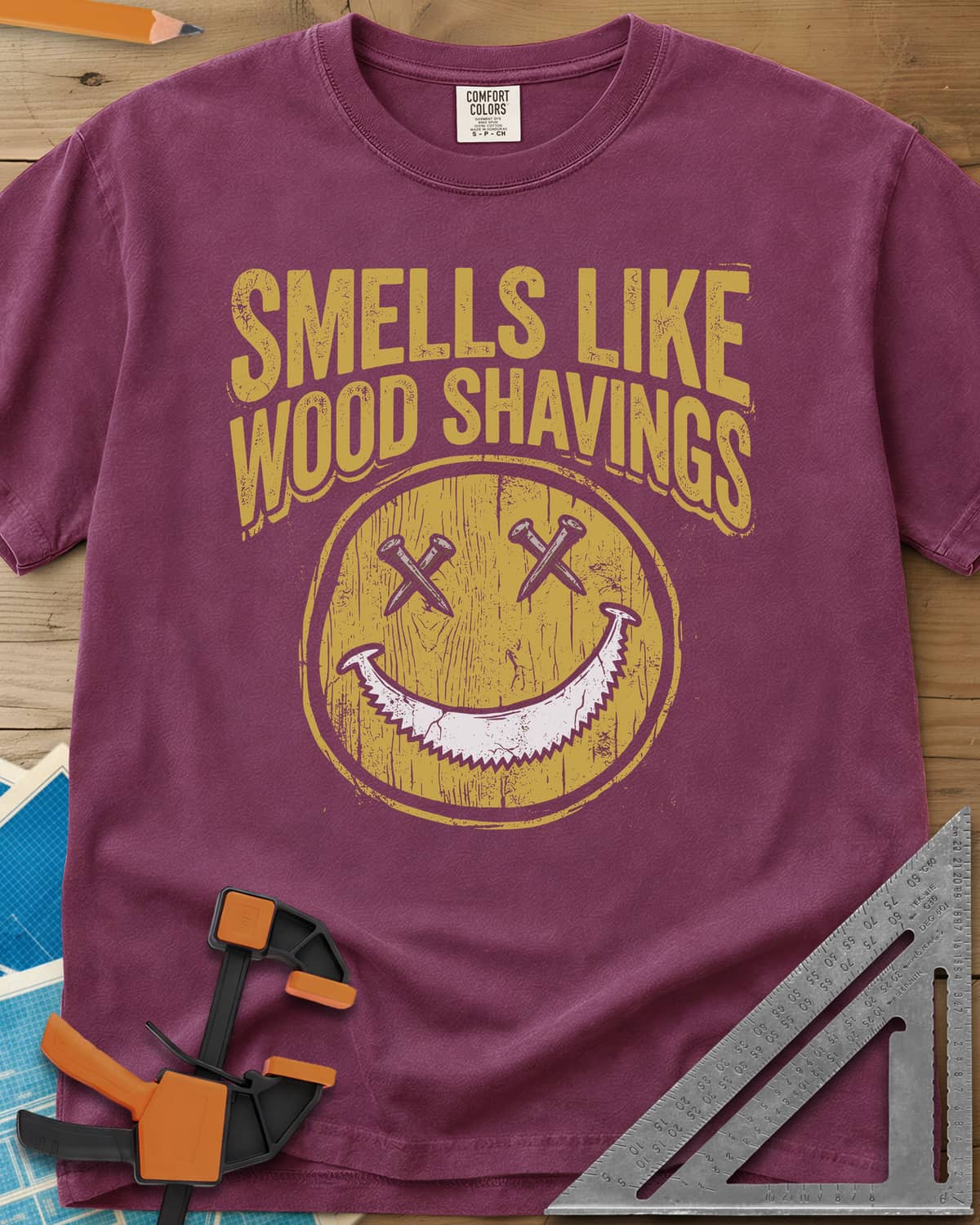 Smells Like Wood Shavings heavyweight tee in Berry, a worn yellow smiley with nails for eyes and a saw blade grin