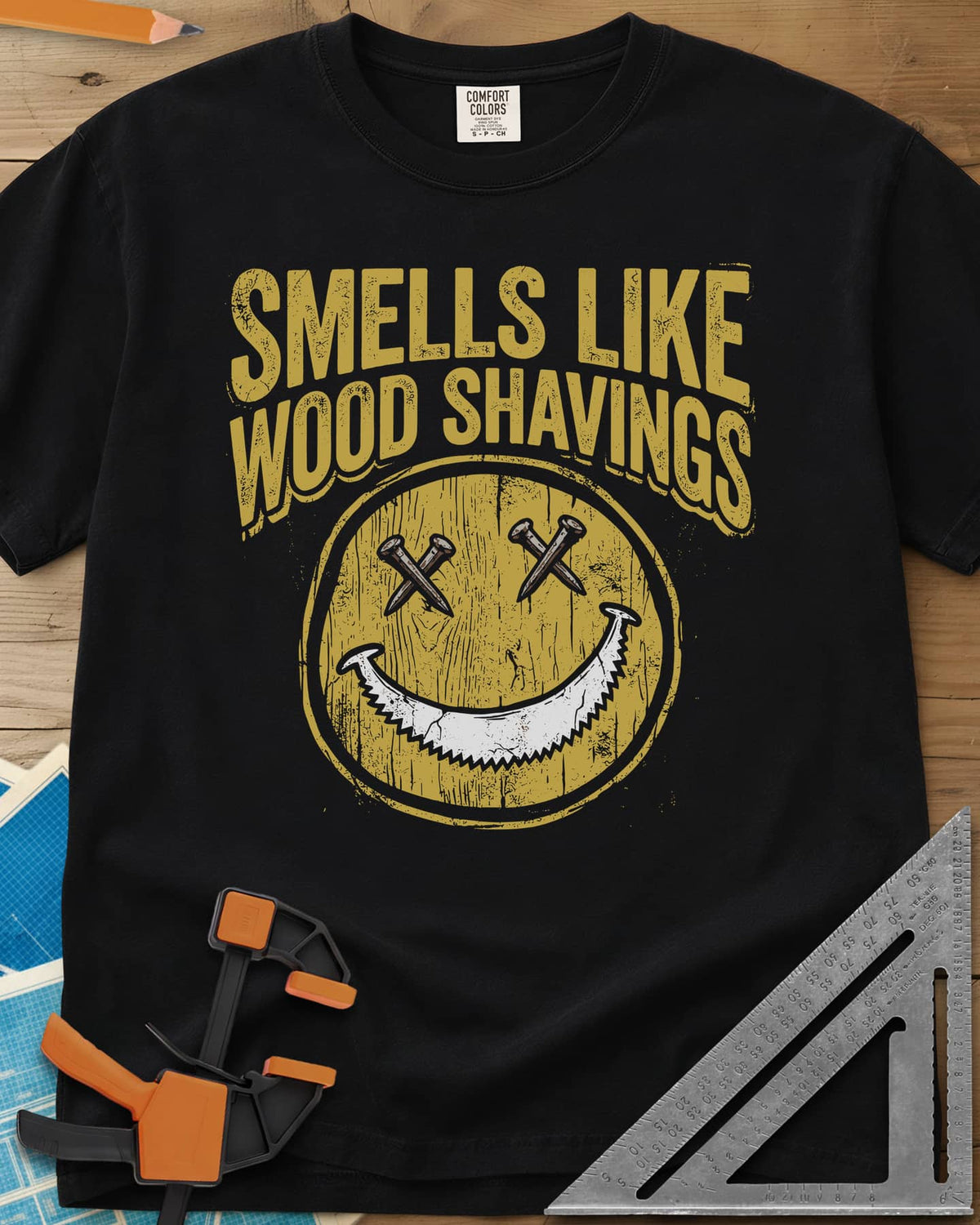 Smells Like Wood Shavings heavyweight tee in Black, a worn yellow smiley with nails for eyes and a saw blade grin