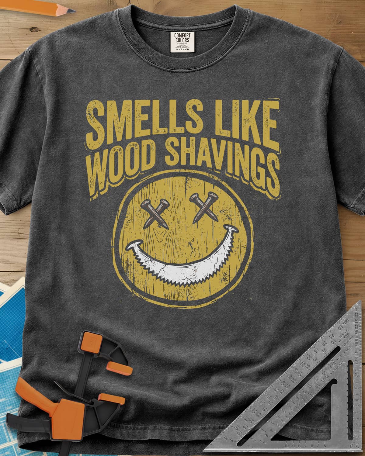Smells Like Wood Shavings heavyweight tee in Pepper, a worn yellow smiley with nails for eyes and a saw blade grin