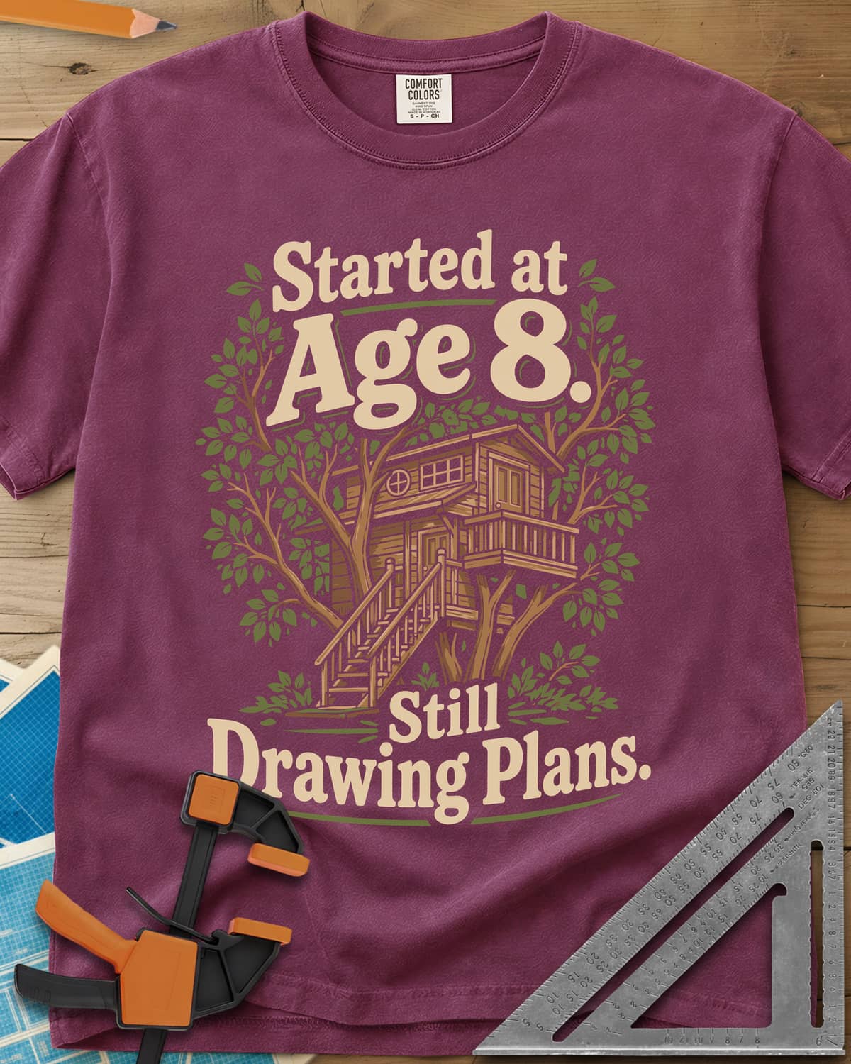 Started At Age 8 heavyweight tee in Berry, a wooden treehouse with a deck and stairs among green leaves