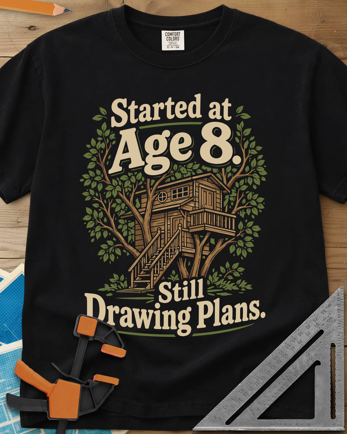Started At Age 8 heavyweight tee in Black, a wooden treehouse with a deck and stairs among green leaves