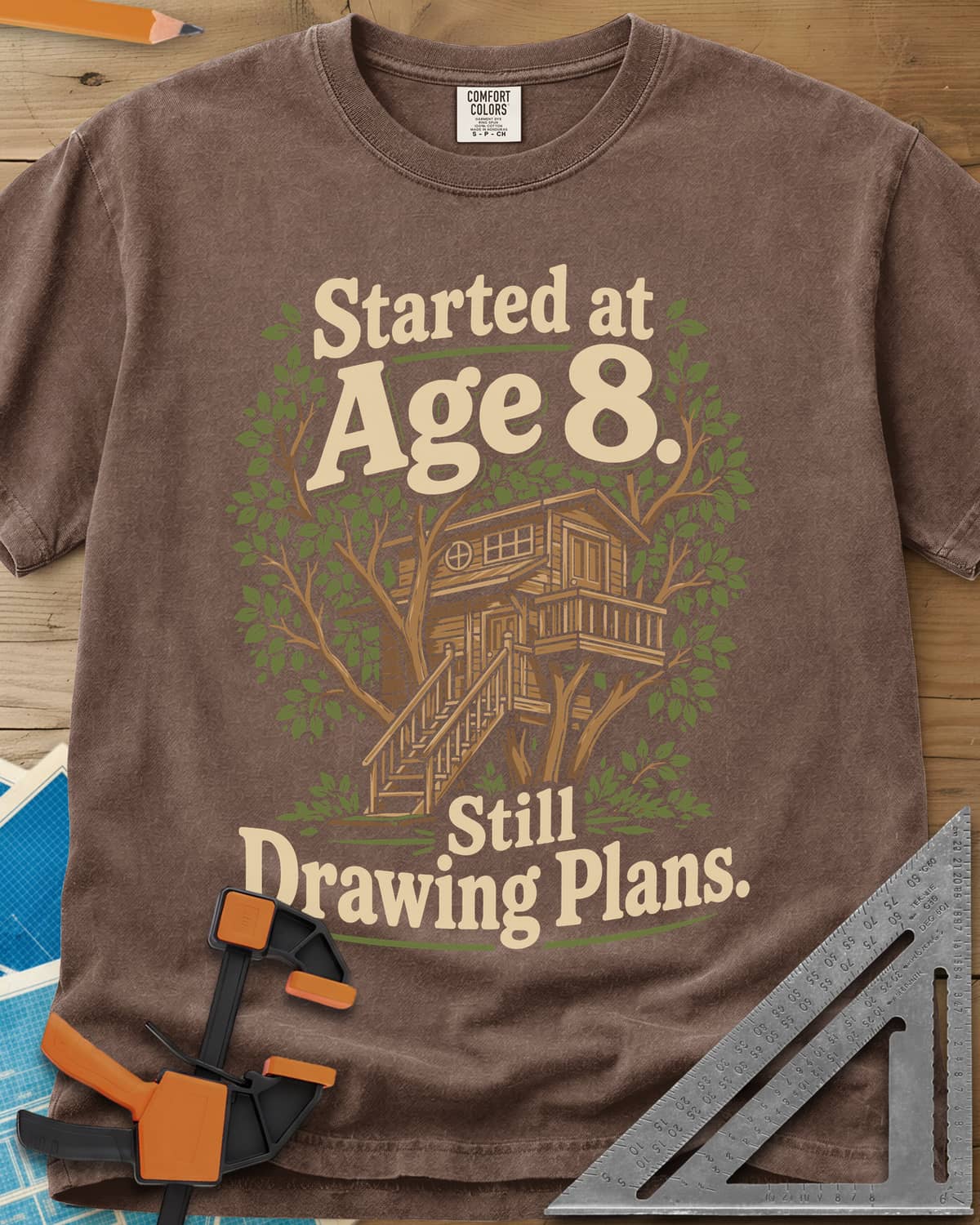Started At Age 8 heavyweight tee in Espresso, a wooden treehouse with a deck and stairs among green leaves