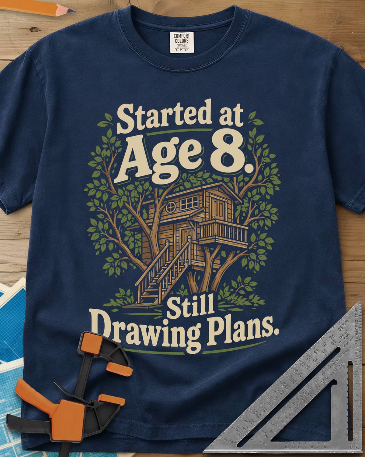 Started At Age 8 heavyweight tee in Navy, a wooden treehouse with a deck and stairs among green leaves