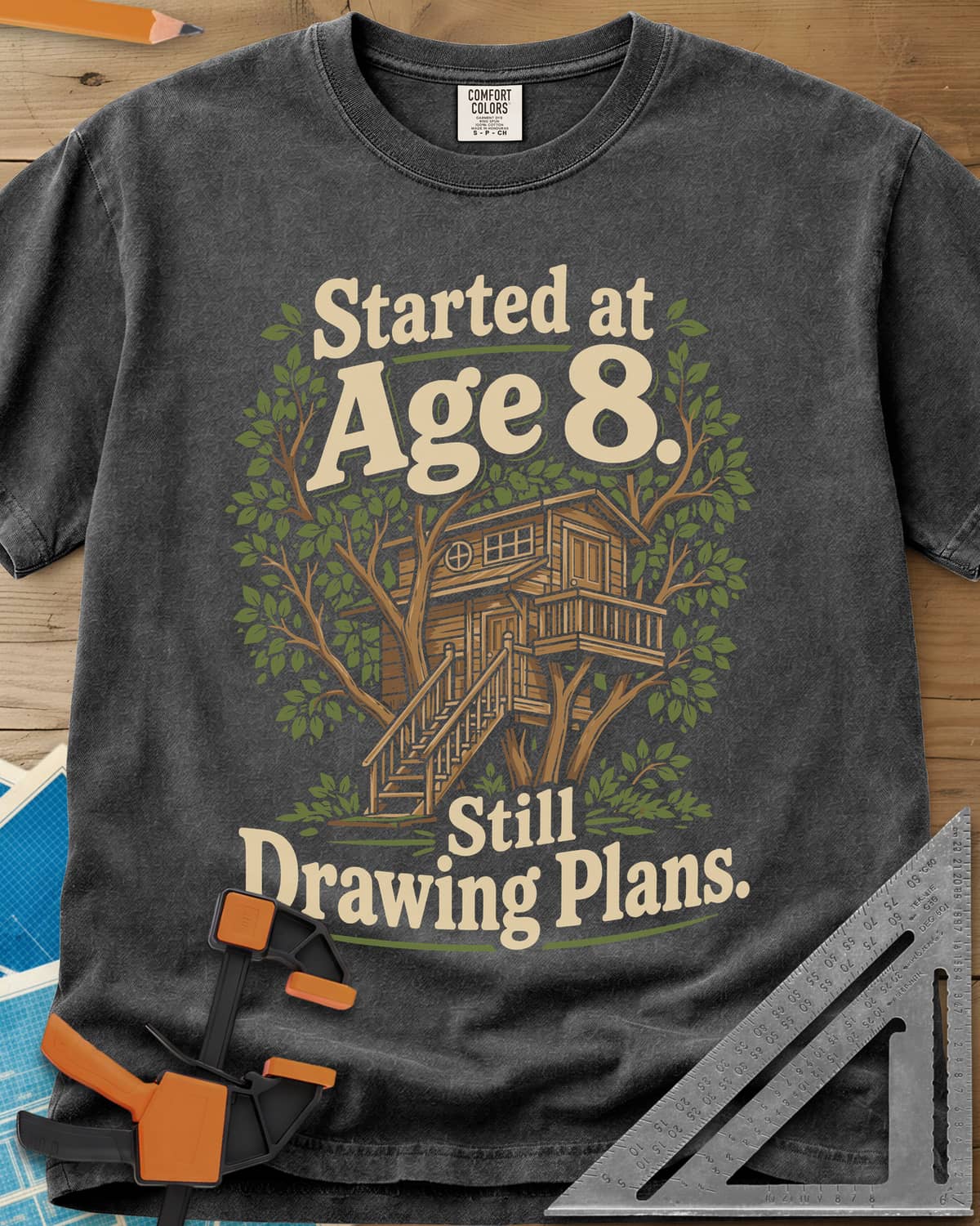 Started At Age 8 heavyweight tee in Pepper, a wooden treehouse with a deck and stairs among green leaves