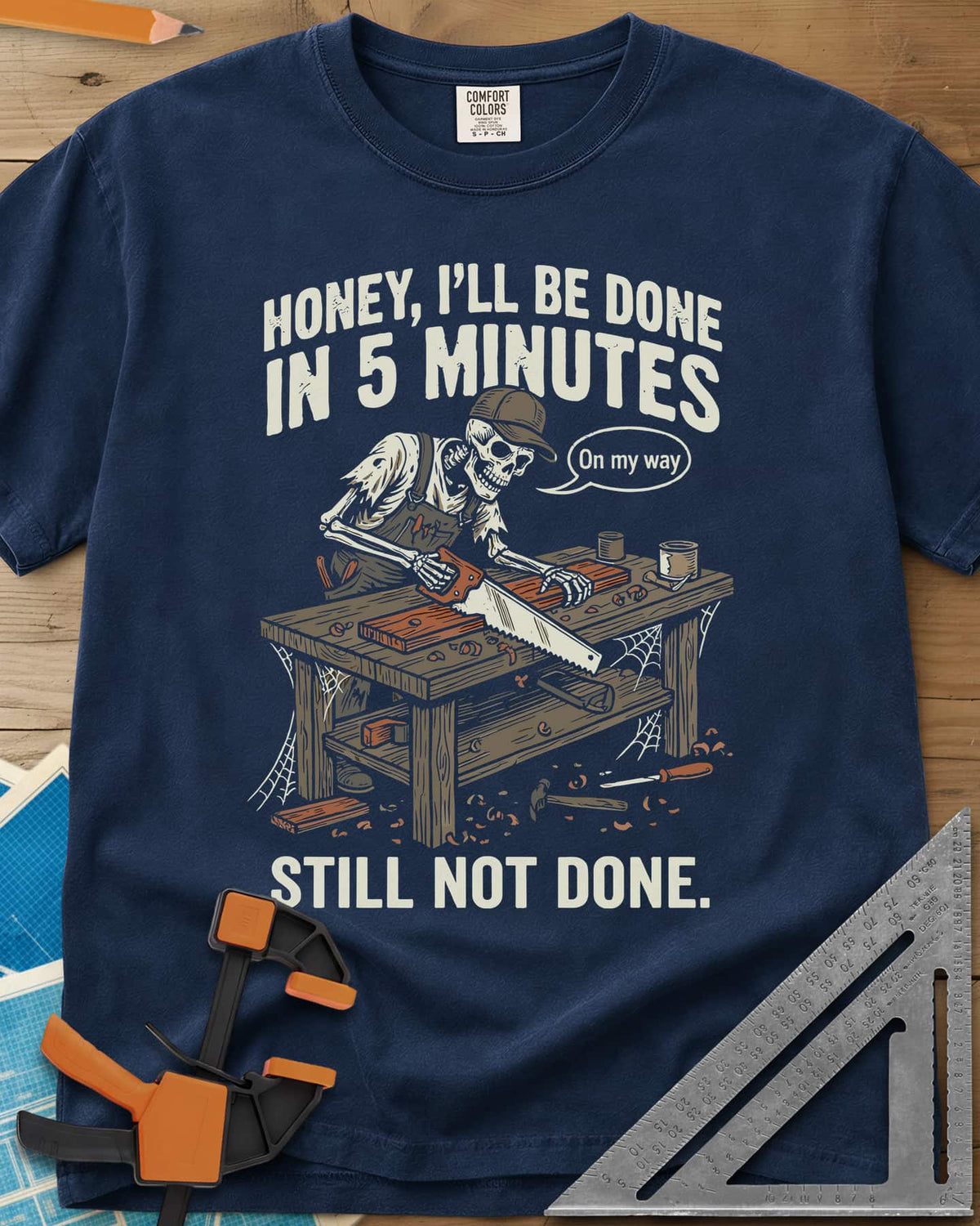 Still Not Done heavyweight tee in Navy, a skeleton in a ball cap sawing a board at a cobwebbed bench