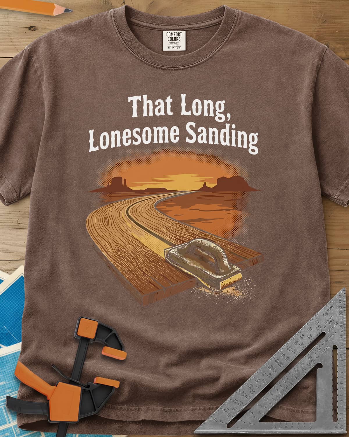 That Long, Lonesome Sanding heavyweight tee in Espresso, a plank road winding through a desert sunset with a sanding block