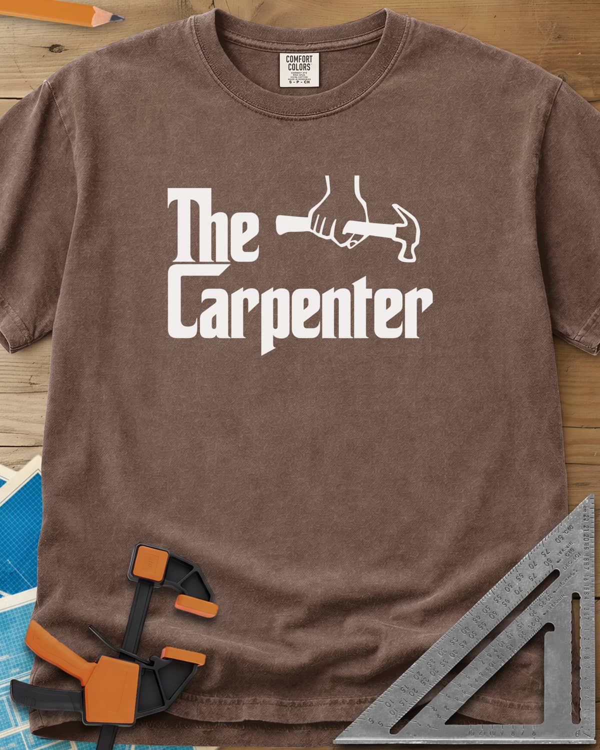 The Carpenter heavyweight tee in Espresso, film-poster style lettering with a fist gripping a hammer