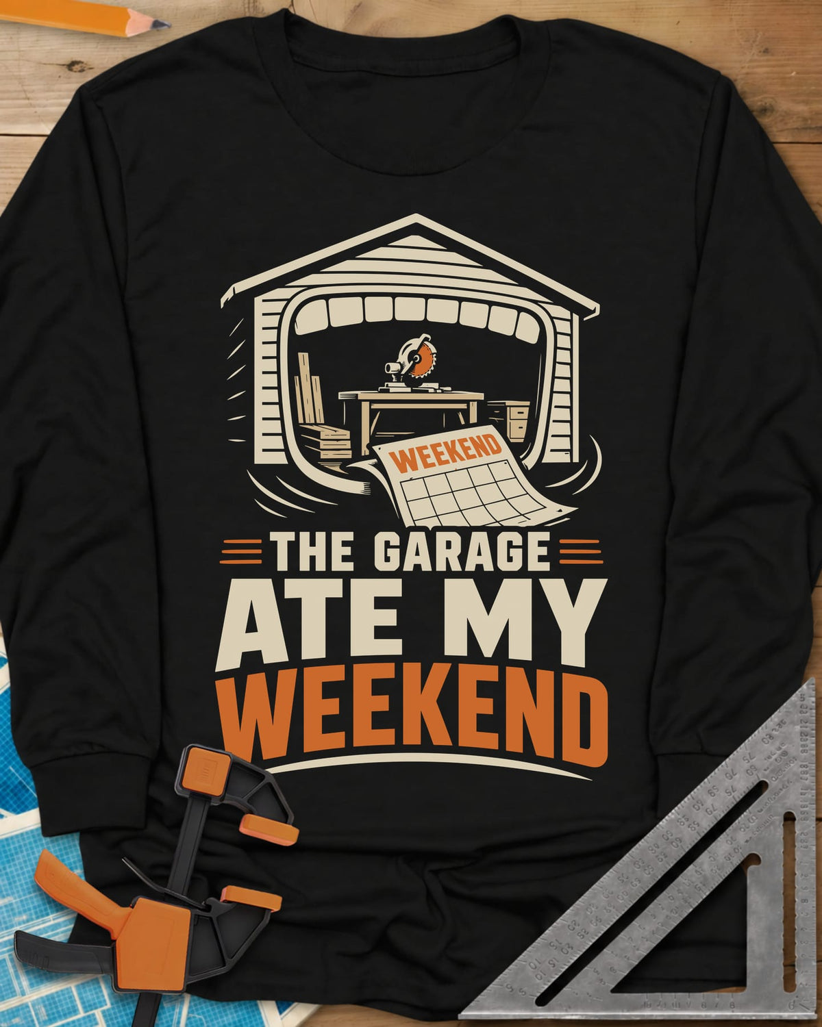 The Garage Ate My Weekend long sleeve shirt in Black, a garage with a miter saw inside and a calendar page flying in