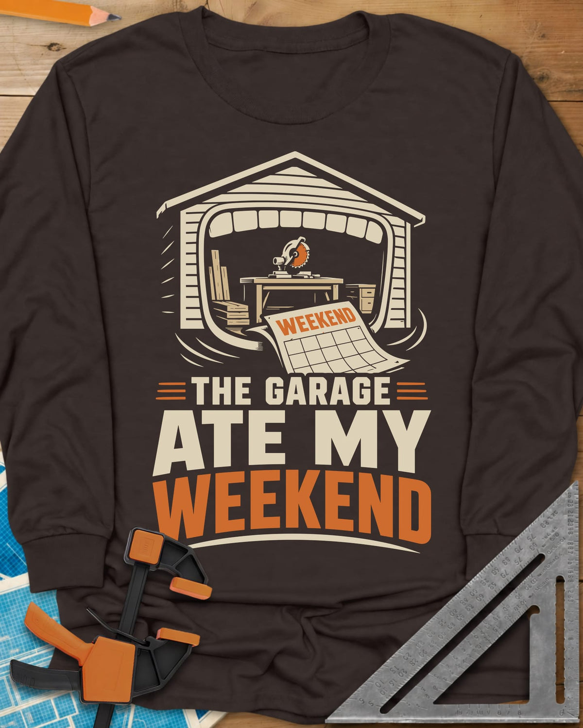 The Garage Ate My Weekend long sleeve shirt in Dark Chocolate, a garage with a miter saw inside and a calendar page flying in