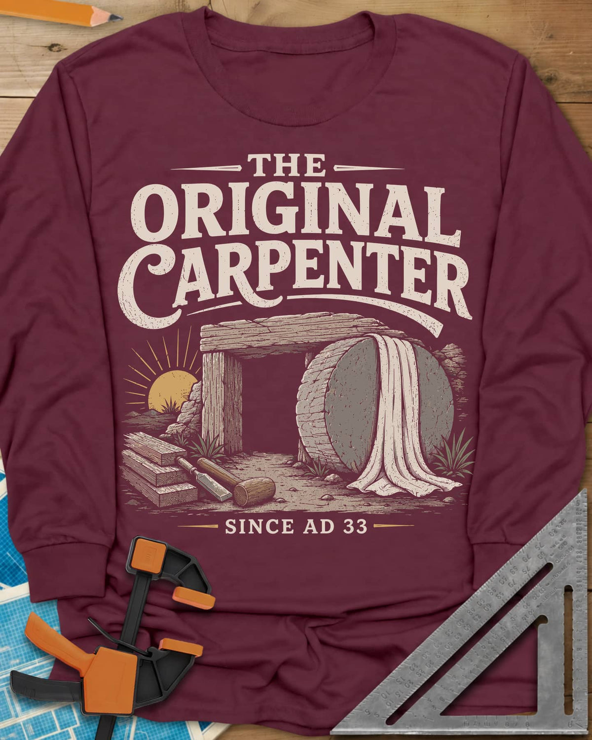 The Original Carpenter long sleeve shirt in Maroon, an empty tomb at sunrise with planks, a mallet and a chisel