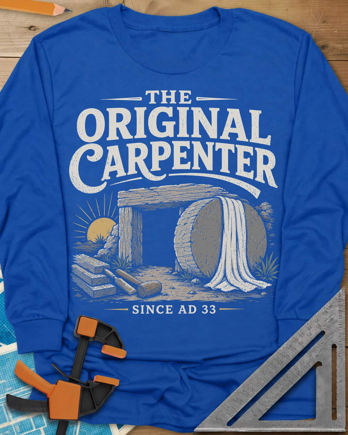 The Original Carpenter long sleeve shirt in Royal, an empty tomb at sunrise with planks, a mallet and a chisel