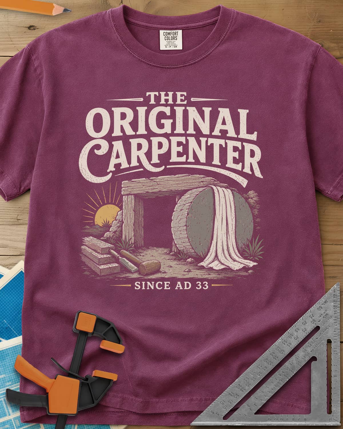 The Original Carpenter heavyweight tee in Berry, an empty tomb at sunrise with planks, a mallet and a chisel