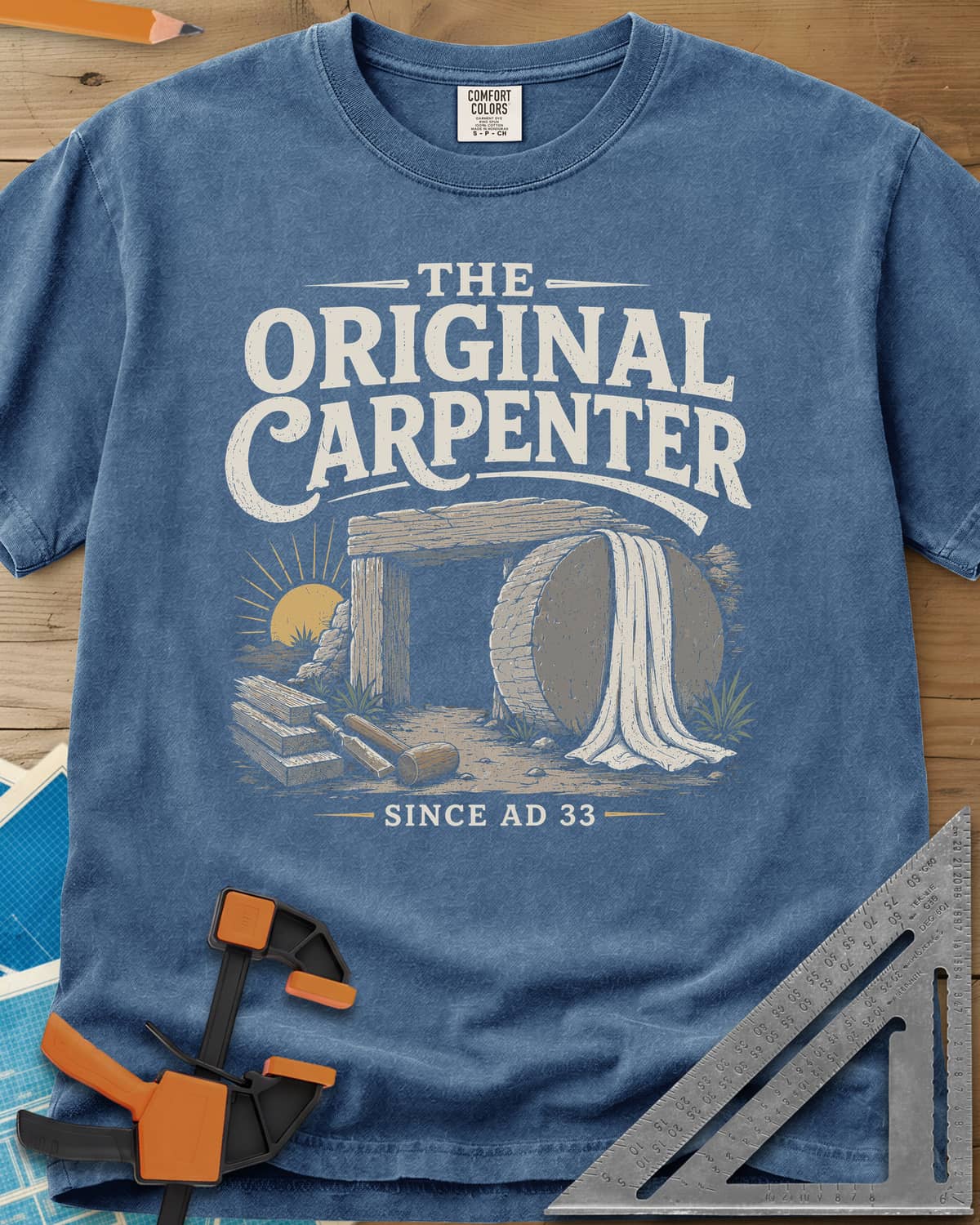 The Original Carpenter heavyweight tee in Blue Jean, an empty tomb at sunrise with planks, a mallet and a chisel