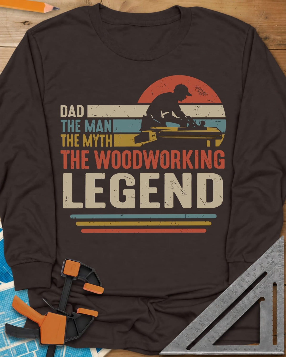 The Woodworking Legend long sleeve shirt in Dark Chocolate, retro sunset stripes behind a silhouetted woodworker at his bench