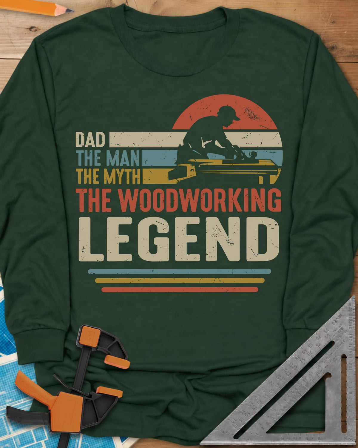 The Woodworking Legend long sleeve shirt in Forest Green, retro sunset stripes behind a silhouetted woodworker at his bench