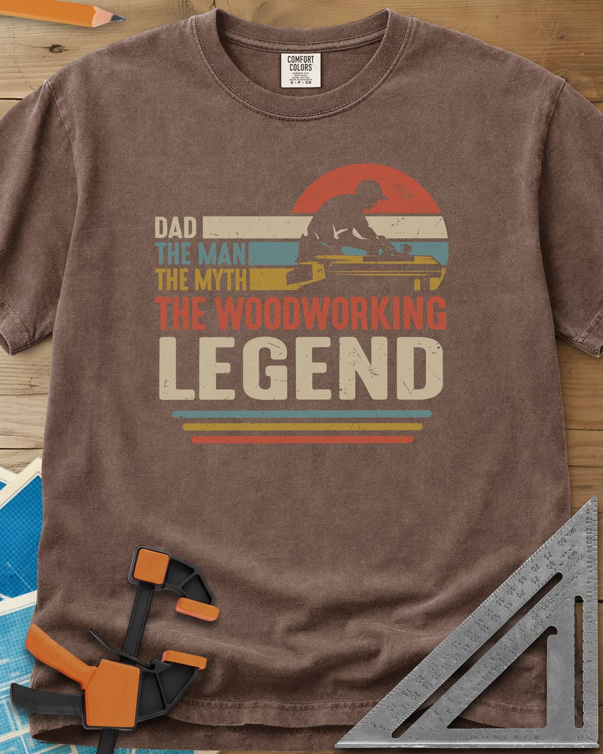 The Woodworking Legend heavyweight tee in Espresso, retro sunset stripes behind a silhouetted woodworker at his bench