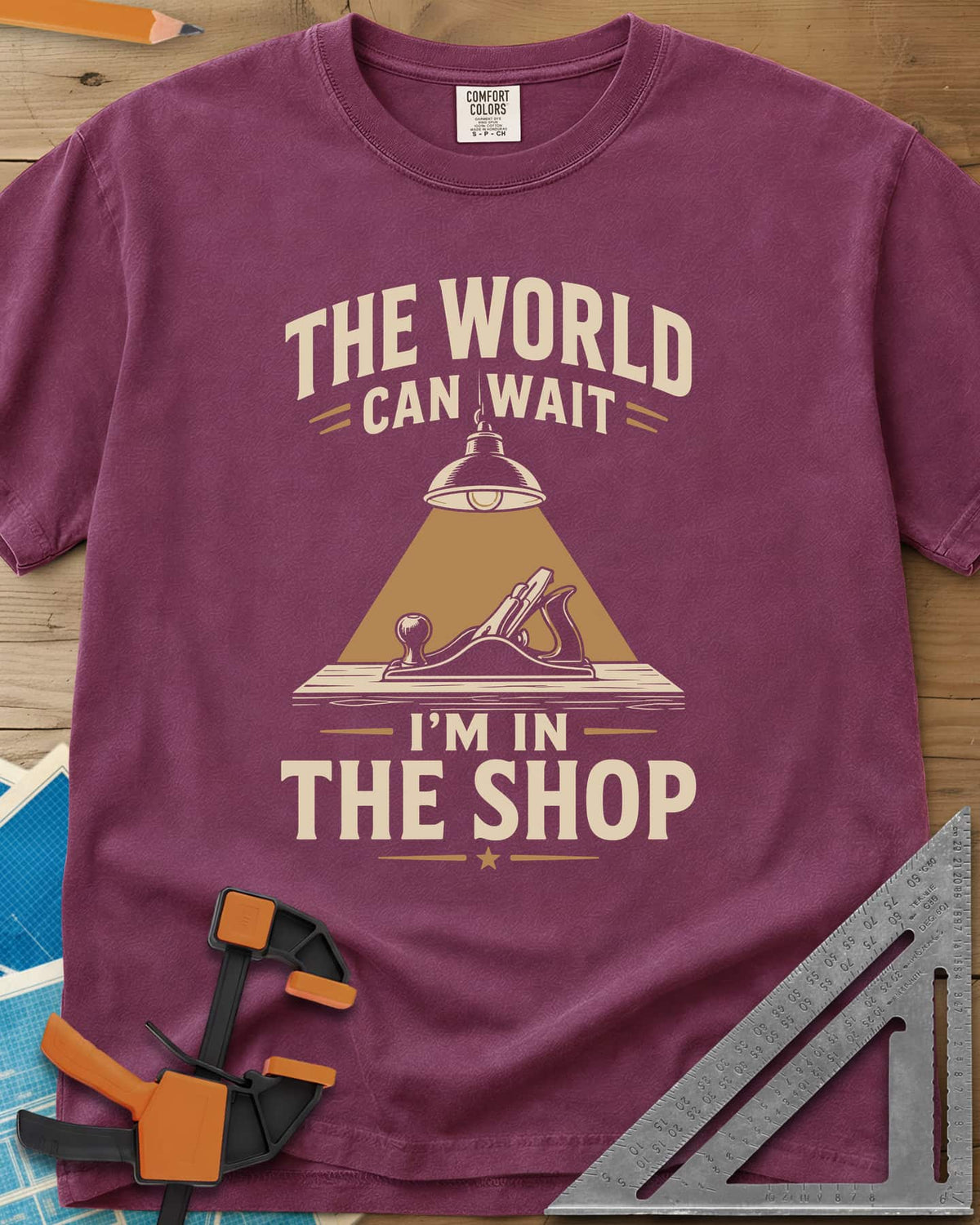 The World Can Wait I'm In The Shop heavyweight tee in Berry, a hand plane under a hanging shop lamp's cone of light