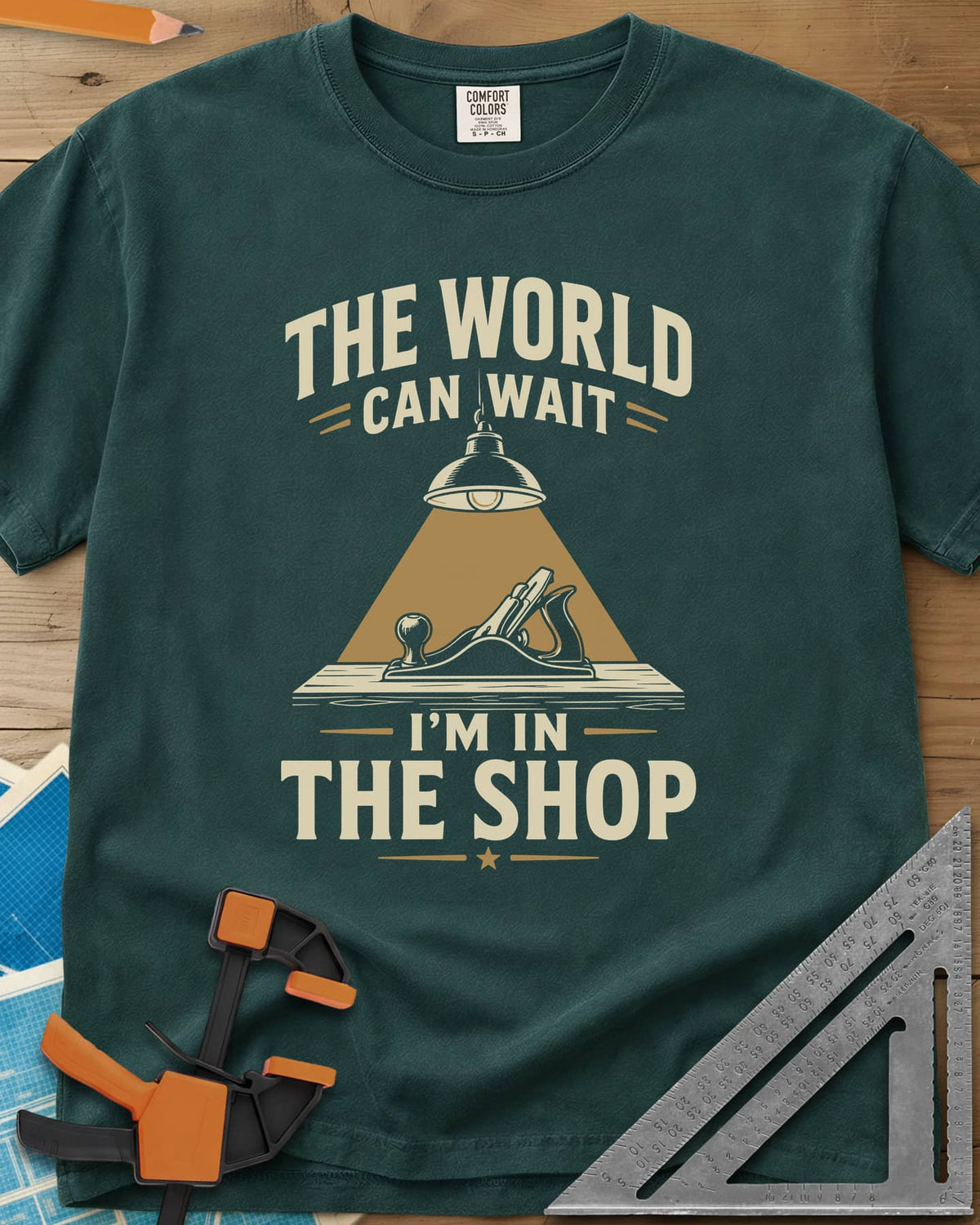 The World Can Wait I'm In The Shop heavyweight tee in Blue Spruce, a hand plane under a hanging shop lamp's cone of light