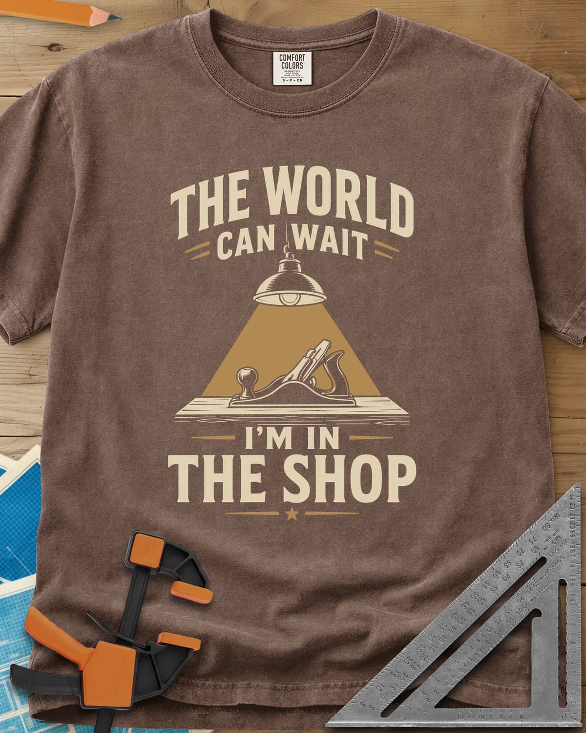 The World Can Wait I'm In The Shop heavyweight tee in Espresso, a hand plane under a hanging shop lamp's cone of light