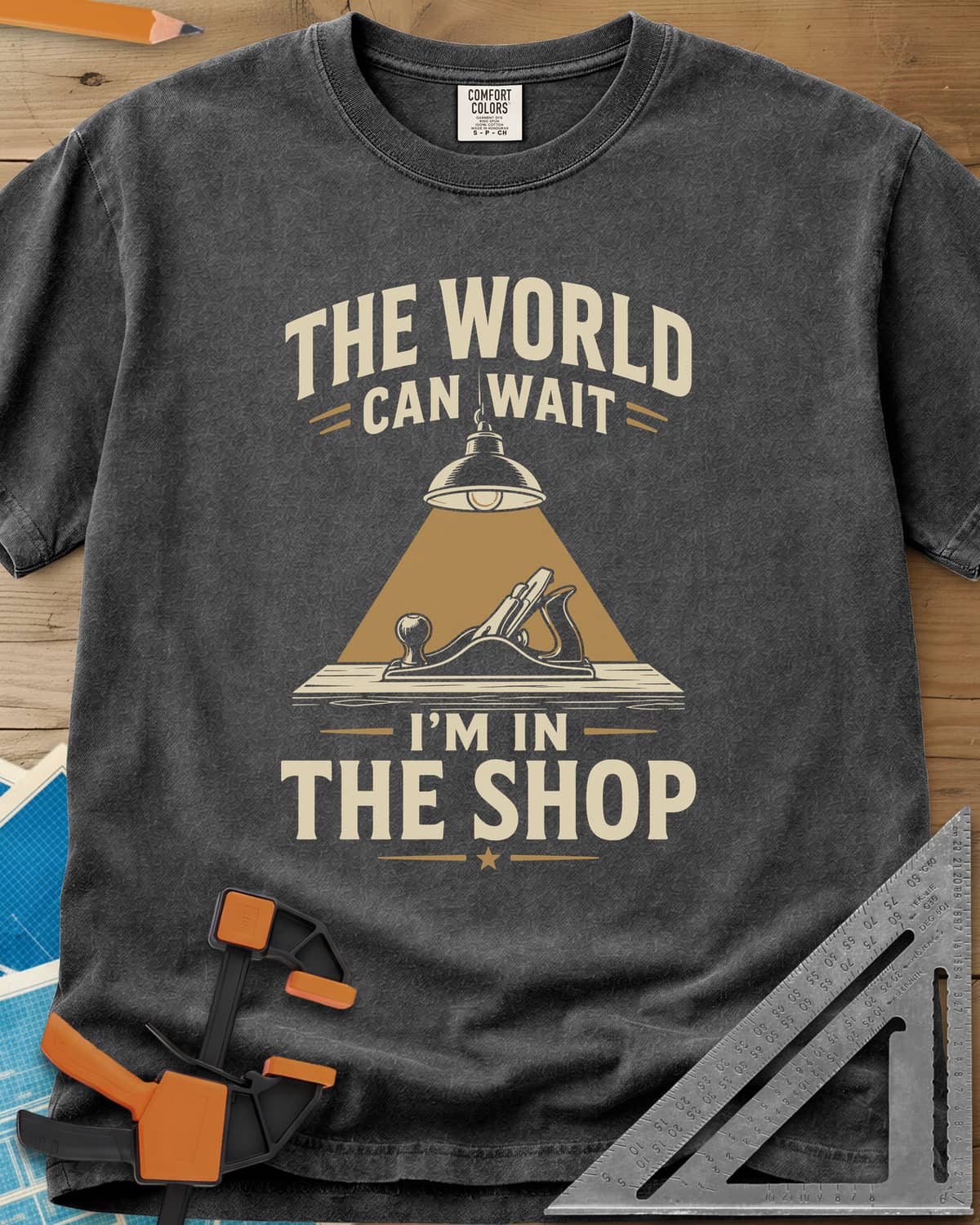The World Can Wait I'm In The Shop heavyweight tee in Pepper, a hand plane under a hanging shop lamp's cone of light