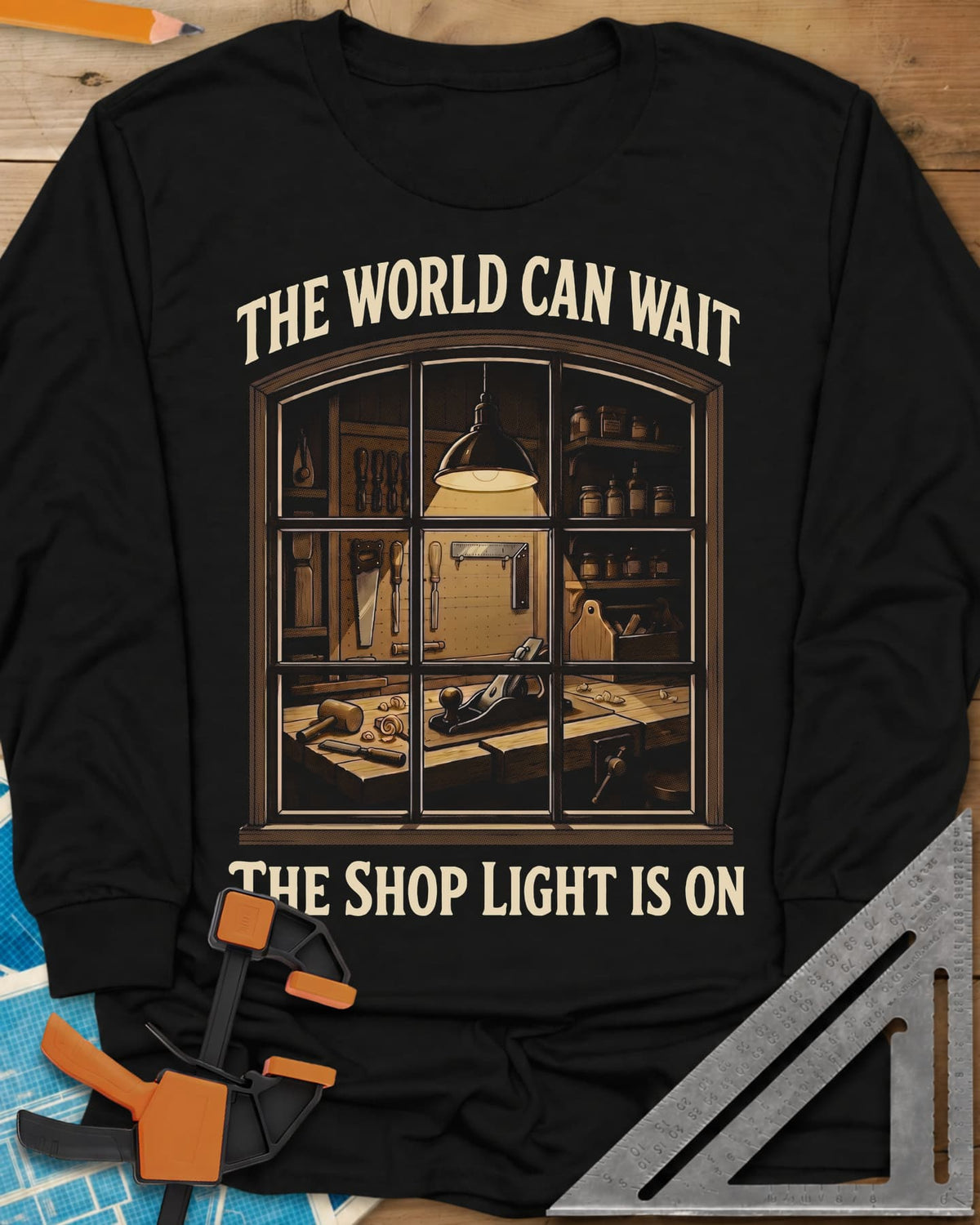 The World Can Wait The Shop Light Is On long sleeve shirt in Black, a lit workshop window: hanging lamp, pegboard, hand