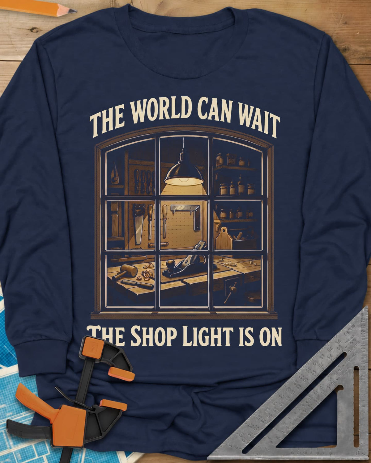 The World Can Wait The Shop Light Is On long sleeve shirt in Navy, a lit workshop window: hanging lamp, pegboard, hand plane
