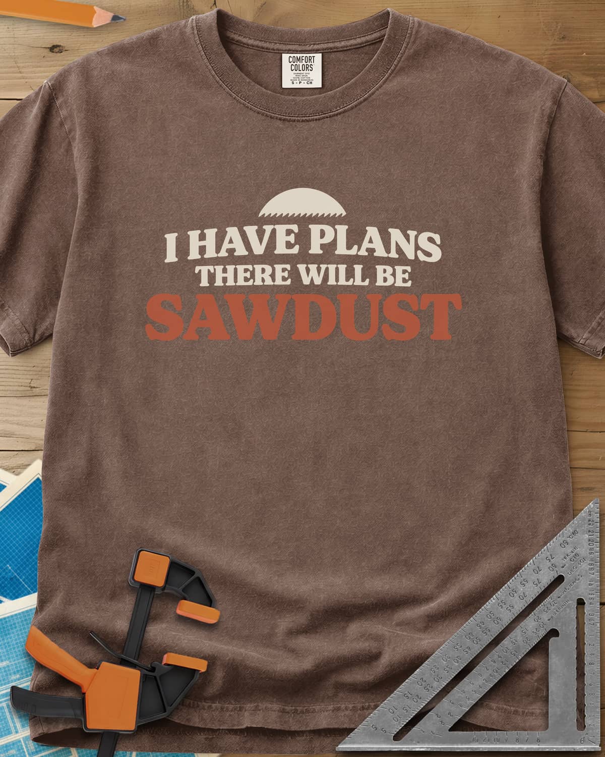 There Will Be Sawdust heavyweight tee in Espresso, half a toothed saw blade above rounded, bold lettering