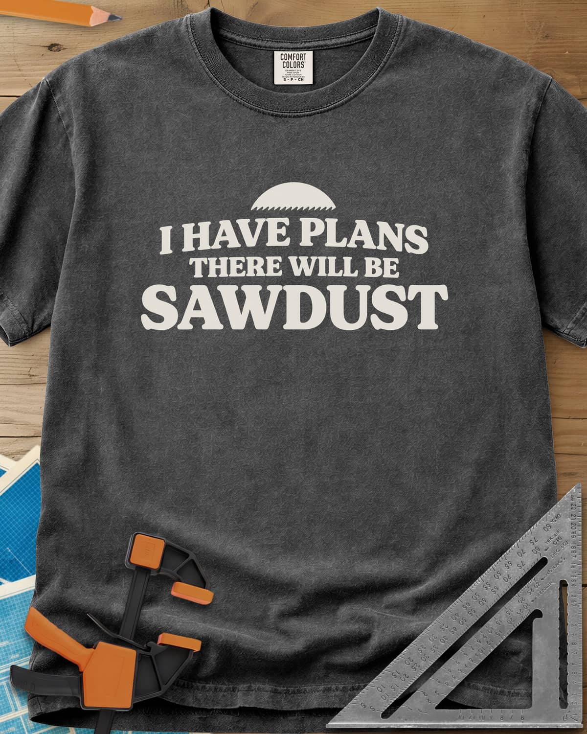 There Will Be Sawdust heavyweight tee in Pepper, half a toothed saw blade above rounded, bold lettering