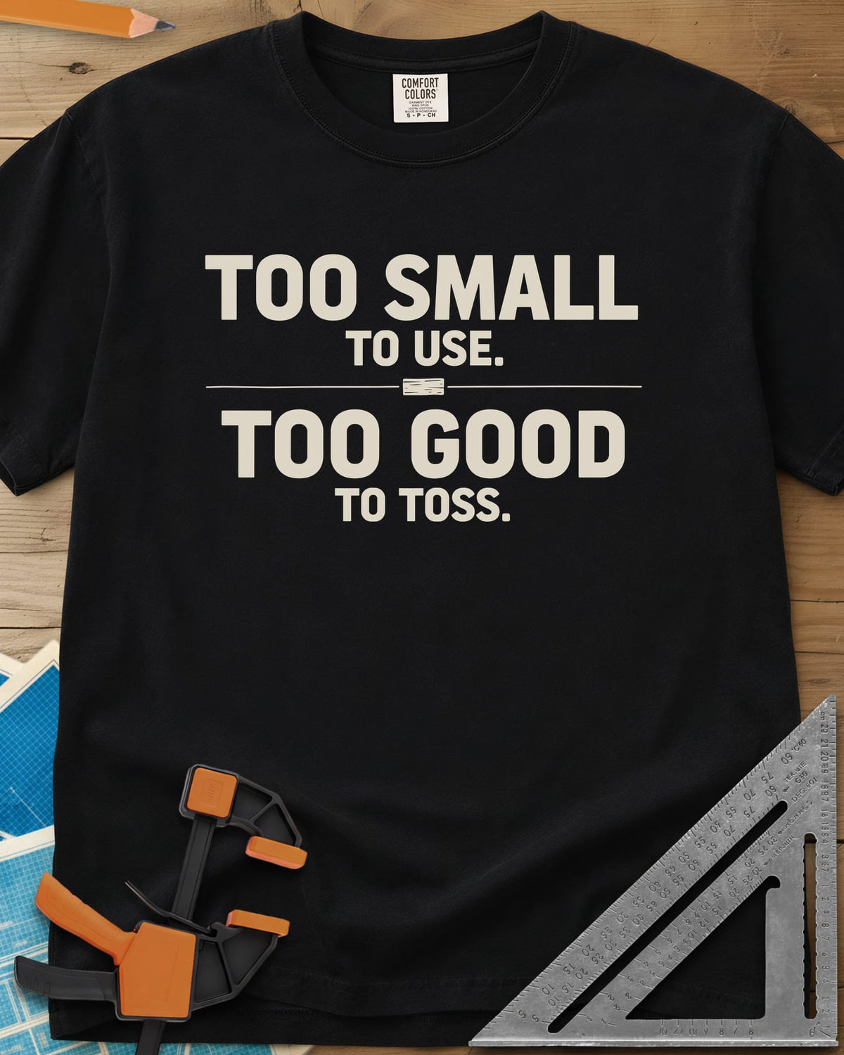 Too Small To Use Too Good To Toss heavyweight tee in Black, two-line slogan split by a rule with a tiny wood offcut