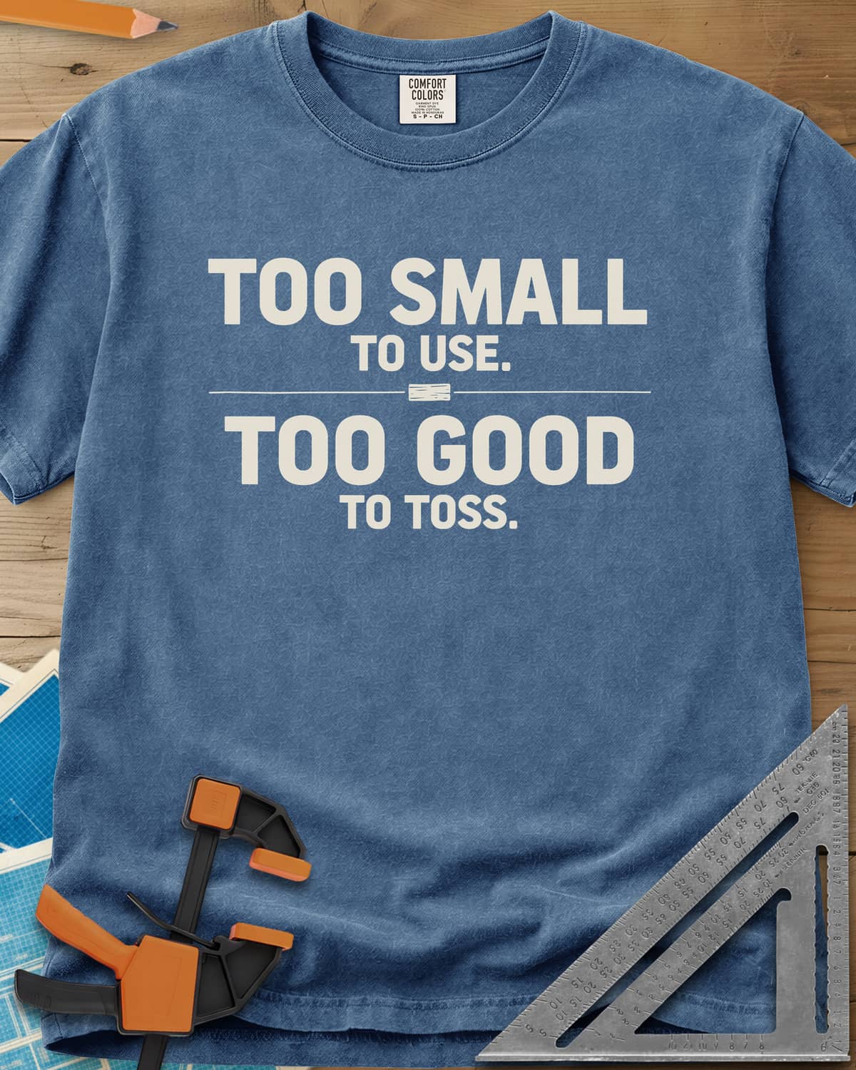 Too Small To Use Too Good To Toss heavyweight tee in Blue Jean, two-line slogan split by a rule with a tiny wood offcut