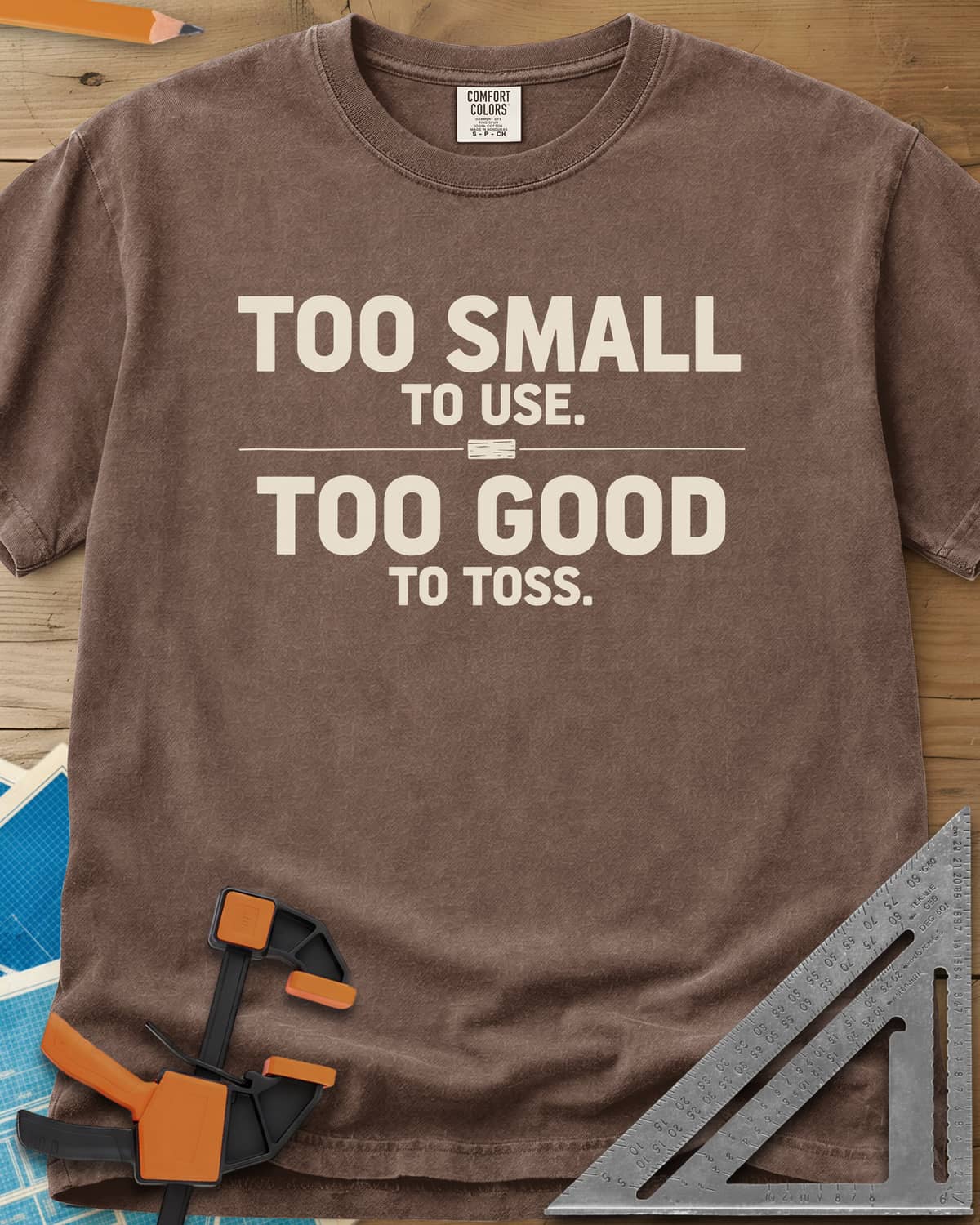Too Small To Use Too Good To Toss heavyweight tee in Espresso, two-line slogan split by a rule with a tiny wood offcut