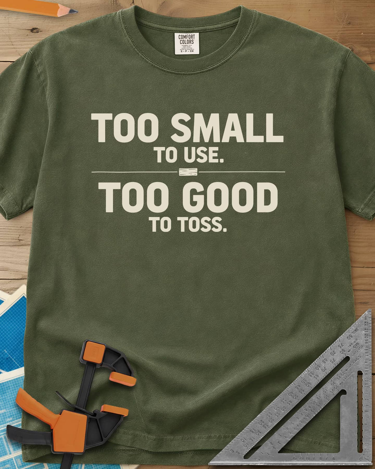 Too Small To Use Too Good To Toss heavyweight tee in Hemp, two-line slogan split by a rule with a tiny wood offcut