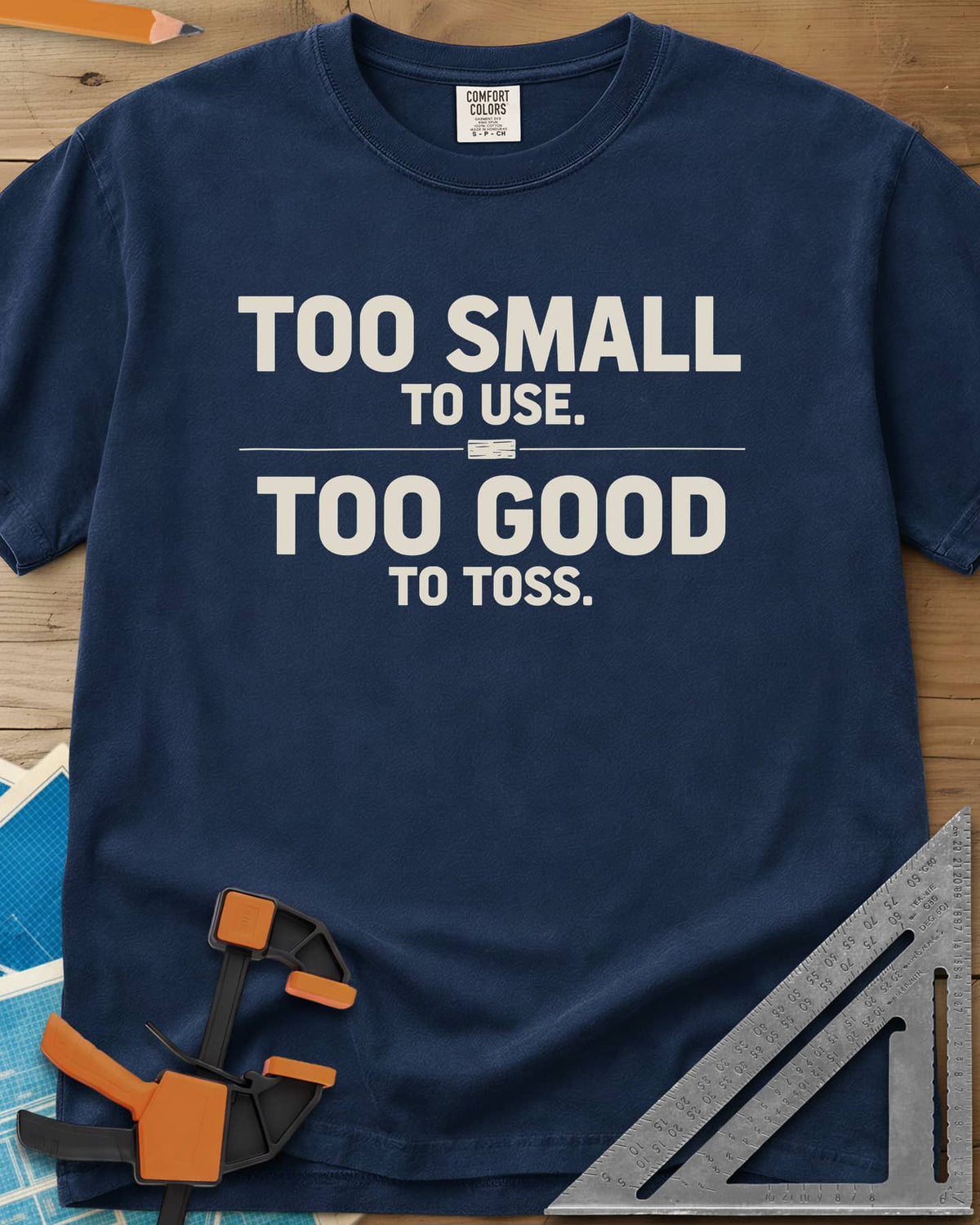 Too Small To Use Too Good To Toss heavyweight tee in Navy, two-line slogan split by a rule with a tiny wood offcut
